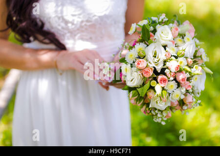 Bride holding a bouquet de mariage avec des roses sur fond vert au cours de l'été Banque D'Images