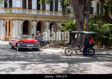 Les touristes de voitures un classique US vintage classic taxi alors qu'un conducteur de pousse-pousse l'air sur la région de Centro Havana Cuba Banque D'Images