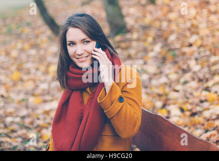 Young woman using mobile phone in autumn park Banque D'Images