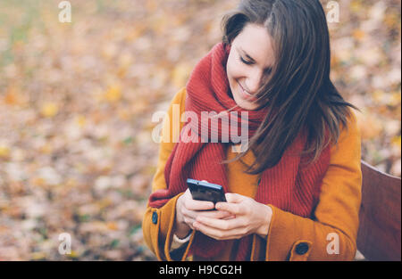 Young woman using mobile phone in autumn park Banque D'Images