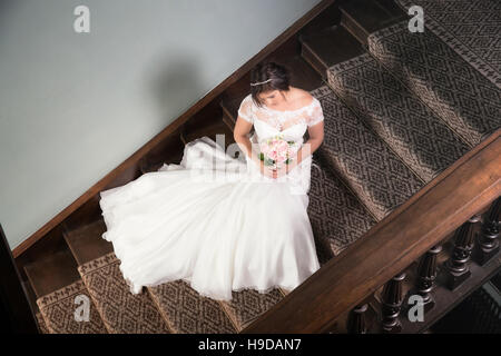 Mariée assise sur l'escalier avec sa robe de mariage se déploient en Banque D'Images