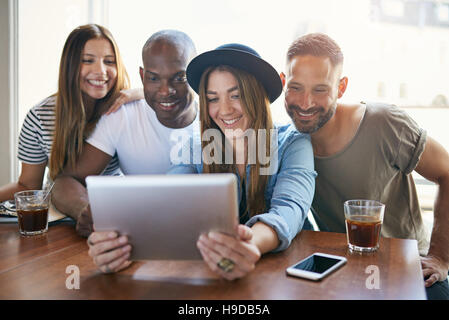 Groupe de quatre jeune collègues assis à table et de partager quelque chose sur les tablettes à la lumière. Banque D'Images