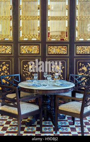 Une table de salle à manger en face d'un Chinois peranakan (Détroit) de la feuille d'or à l'écran au Restaurant Kebaya Sept Terrasses Hôtel à George Town, Penang, Malaysi Banque D'Images