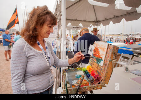 Une femme de race blanche artiste marin travaille à son chevalet dans un Newport Beach, CA, yacht club yacht yard représentant un navire dans le port. Remarque Les peintures colorées. Banque D'Images