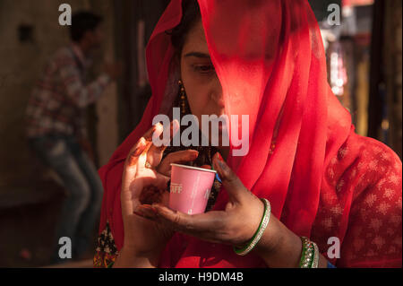 Femme rajasthani couverts face avec voile rouge, et de boire du thé en Inde Rajasthan Pushkar foire Banque D'Images