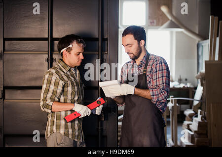 Happy male carpenter montrant quelque chose à un collègue règle et d'ordinateur portable d'atelier Banque D'Images