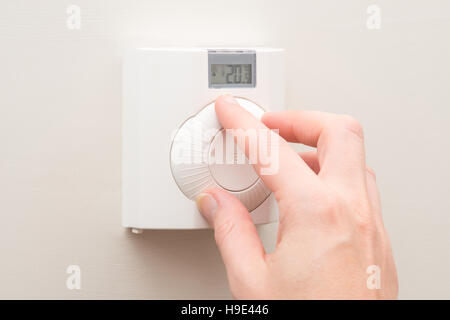 Une main tourne le cadran sur un mur blanc thermostat monté la température de 20 degrés de lecture Banque D'Images