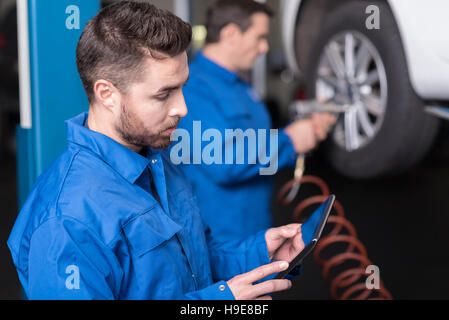 Jeune mécanicien de voiture à l'aide de tablet Banque D'Images