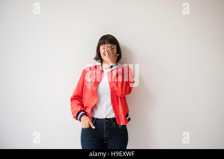 Laughing woman wearing red jacket leaning on wall Banque D'Images