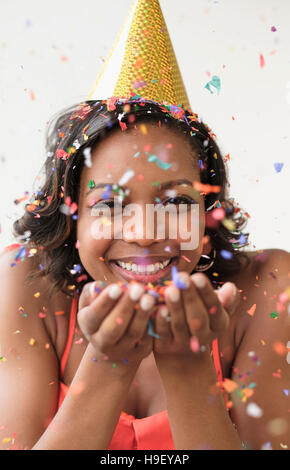 Mixed Race woman wearing party hat blowing confetti Banque D'Images