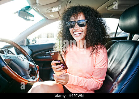Laughing Caucasian woman in car holding texting on cell phone Banque D'Images