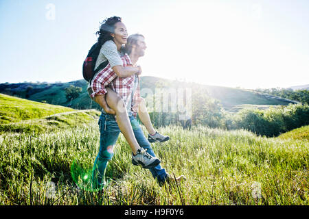 Smiling Man carrying girlfriend piggyback sur hill Banque D'Images