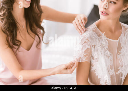 Souriante jeune demoiselle d'aider la mariée avec sa robe Banque D'Images