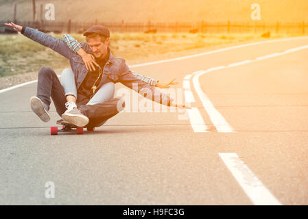 Le gars avec la fille de route de longboard sur une route de montagne. Woman hugging man. Leurs mains se sont séparées en différentes directions. Banque D'Images