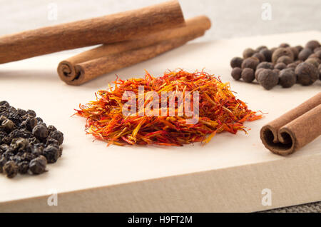 Les relishs et épices - Les bâtons de cannelle, de piment de grains, de safran et de grains de poivre sur un plateau en bois avec une faible profondeur de foyer. Banque D'Images
