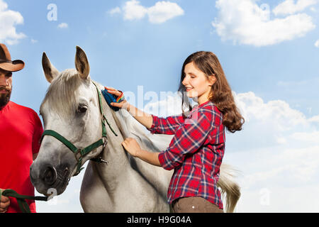 Jeune femme de la crinière de toilettage son cheval blanc Banque D'Images