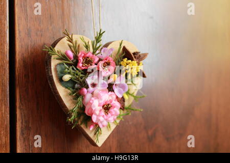 Coeur en bois orné de fleurs artificielles accroché sur la porte de placard Banque D'Images