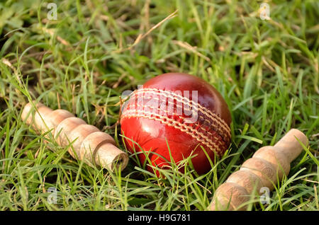 Cricket ball en cuir rouge et passants sur l'herbe Banque D'Images