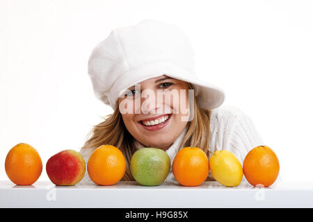 Jeune femme portant un cavalier blanc et un chapeau derrière les pommes, oranges et un citron Banque D'Images
