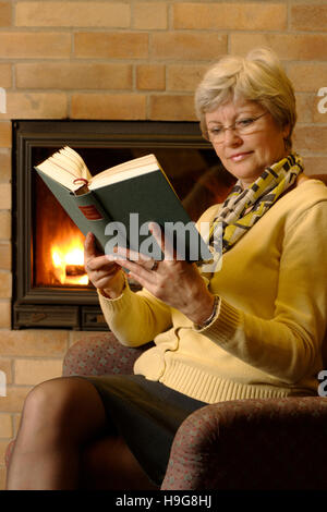 Femme lisant un livre à une cheminée Banque D'Images