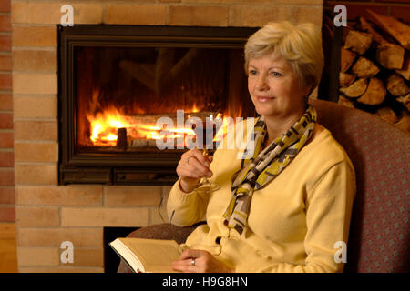 Femme avec du vin rouge de la lecture d'un livre à une cheminée Banque D'Images