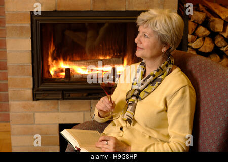 Femme avec du vin rouge de la lecture d'un livre à une cheminée Banque D'Images
