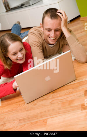 Couple allongé sur le plancher du salon, travailler sur un ordinateur portable Banque D'Images