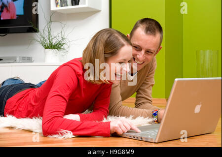 Couple allongé sur le plancher du salon, travailler sur un ordinateur portable Banque D'Images