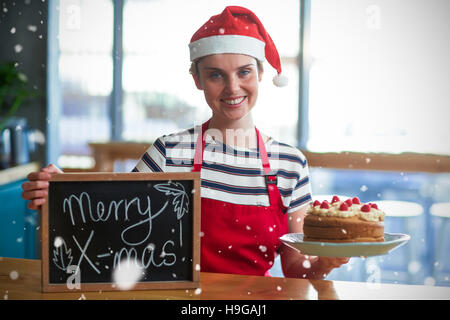 Composite image of waitress holding ardoise avec merry x-mas sign and cake Banque D'Images