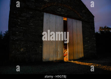 La lumière brille à partir de la moitié des portes ouvertes d'une vieille grange en pierre dans la nuit irlandaise Banque D'Images