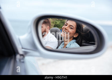 Belle femme souriante à son reflet dans un miroir de voiture Banque D'Images