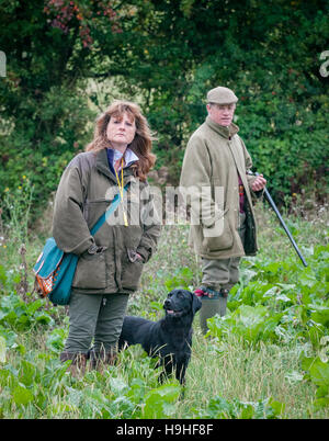 Une gent avec un fusil et une dame avec un chien labrador noir sur un faisan ou perdrix shoot Banque D'Images