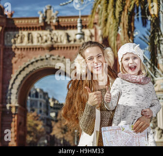 À Barcelone pour un hiver parfait. Portrait of smiling trendy la mère et l'enfant près de Arc de Triomf de Barcelone, Espagne avec map showing Thumbs up Banque D'Images