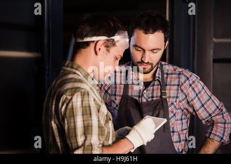 Deux charpentiers parlons en maintenant des documents et règle. L'un d'eux porte un masque de sécurité. Fond atelier de menuiserie Banque D'Images