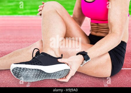 Image composite de l'athlète féminine blessés assis et dépose sa chaussure Banque D'Images