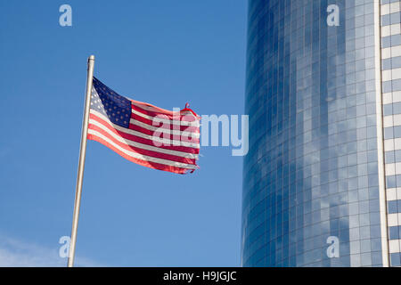 Stars and Stripes Flag s'agite à côté d'un gratte-ciel moderne à la façade de verre dans le quartier financier de Manhattan, New York City. Un effet de flou sur l'ed Banque D'Images