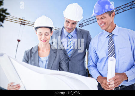 Image composite d'hommes d'affaires et une femme avec un casque et holding blueprint Banque D'Images