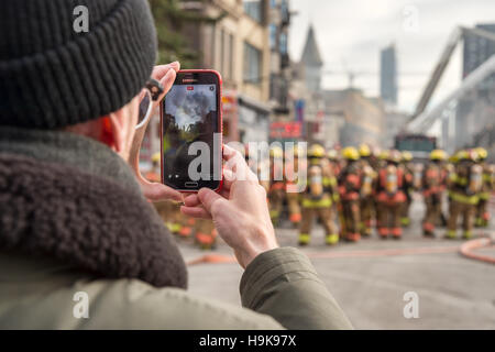 Montréal, ca - 23 nov 2016 : piétons mâles prend des photos avec le smartphone comme les pompiers travaillent sur 'cafe amusement 68' building Banque D'Images