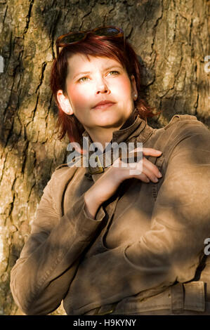 Portrait d'une jeune femme rousse, appuyé contre un tronc d'arbre Banque D'Images