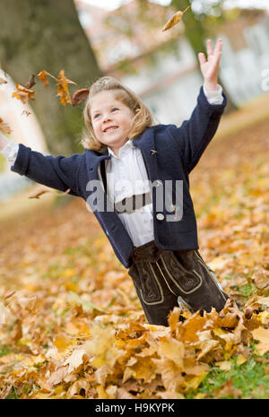 7-year-old girl, jetant le feuillage d'automne Banque D'Images