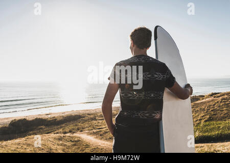 Vue arrière de teenage boy with surfboard à à la mer Banque D'Images