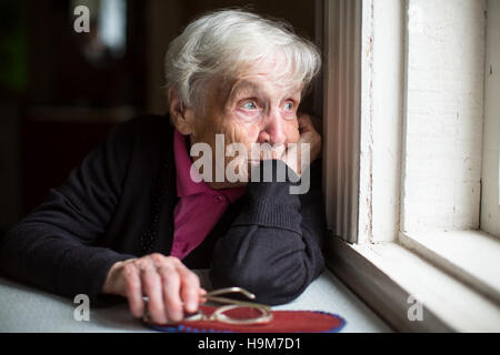Une femme âgée a l'air tristement par la fenêtre. Banque D'Images