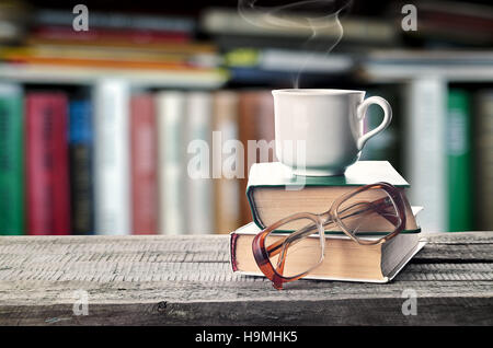 Un café chaud ou un thé, cacao, chocolat cup le livre et lunettes avec copie espace pour le texte sur le fond d'une étagère. Pile de livres Banque D'Images