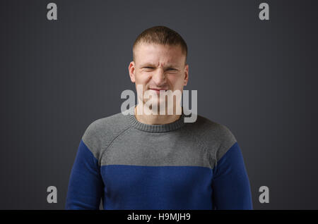 Portrait d'un jeune homme qui n'est pas satisfait de quelque chose. Photo émotionnelle en studio sur un fond noir. Banque D'Images