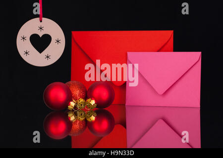 Enveloppes rouges et roses et décoration de Noël sur la table en verre noir Banque D'Images