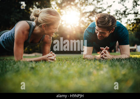 Fit young man and woman exercising in park. Smiling caucasian couple d'entraînement de base sur l'herbe.