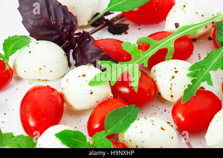 Les tomates avec de la mozzarella, roquette et basilic sur un fond blanc. Banque D'Images