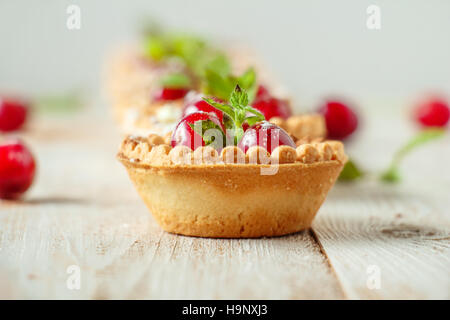 Tartelettes de crème fouettée et de cerises sur un fond de bois blanc. Focus sélectif. Banque D'Images