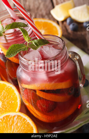 Sangria avec les agrumes, fraises, bleuets et macro dans un bocal en verre sur la table verticale. Banque D'Images