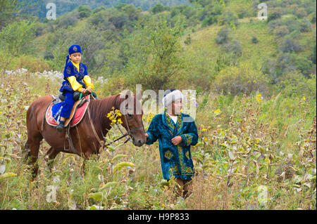 Balades autour de l'homme kazakh avec son fils sur un cheval après la cérémonie de circoncision Sundet Toi, Kazakh village ethnographique Banque D'Images